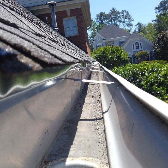 Close-up of a house gutter filled with debris, angled perspective. Sunny outdoor setting.