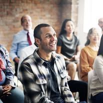 Man in flannel shirt smiles in a group setting with other people.