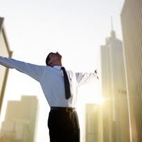 Man in business attire with arms outstretched, celebrating. City skyline backdrop.
