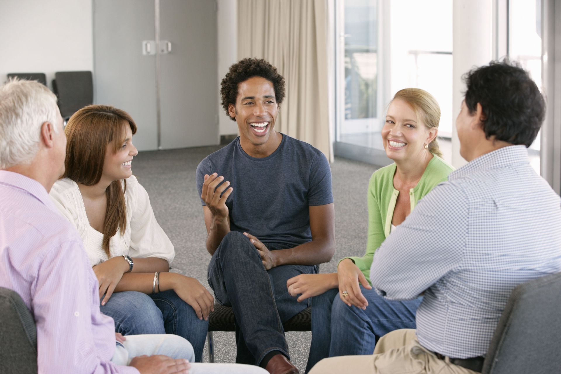 People in a circle, smiling and talking. Informal setting, possibly a support group.
