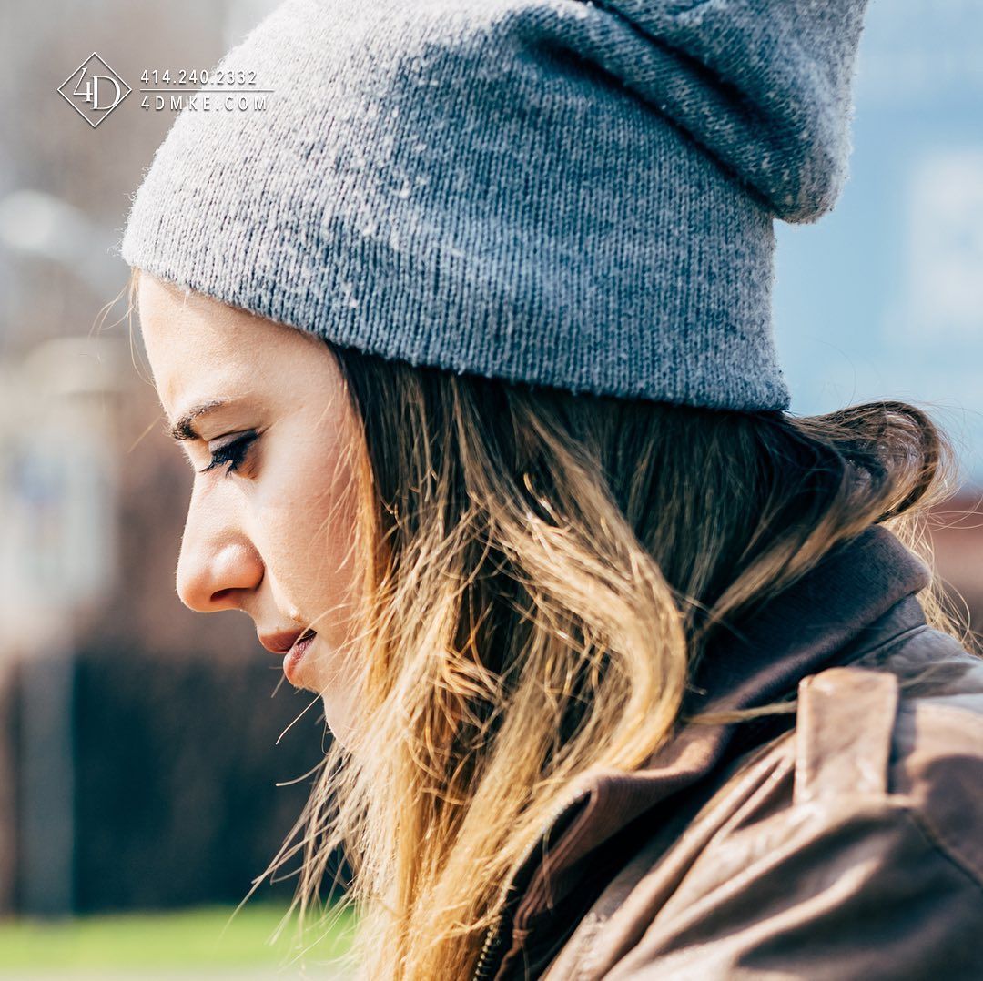 Woman in gray beanie and leather jacket, looking down thoughtfully, outdoors.
