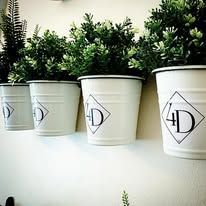 Four white planters with greenery, mounted on a white wall. Each pot has a logo.