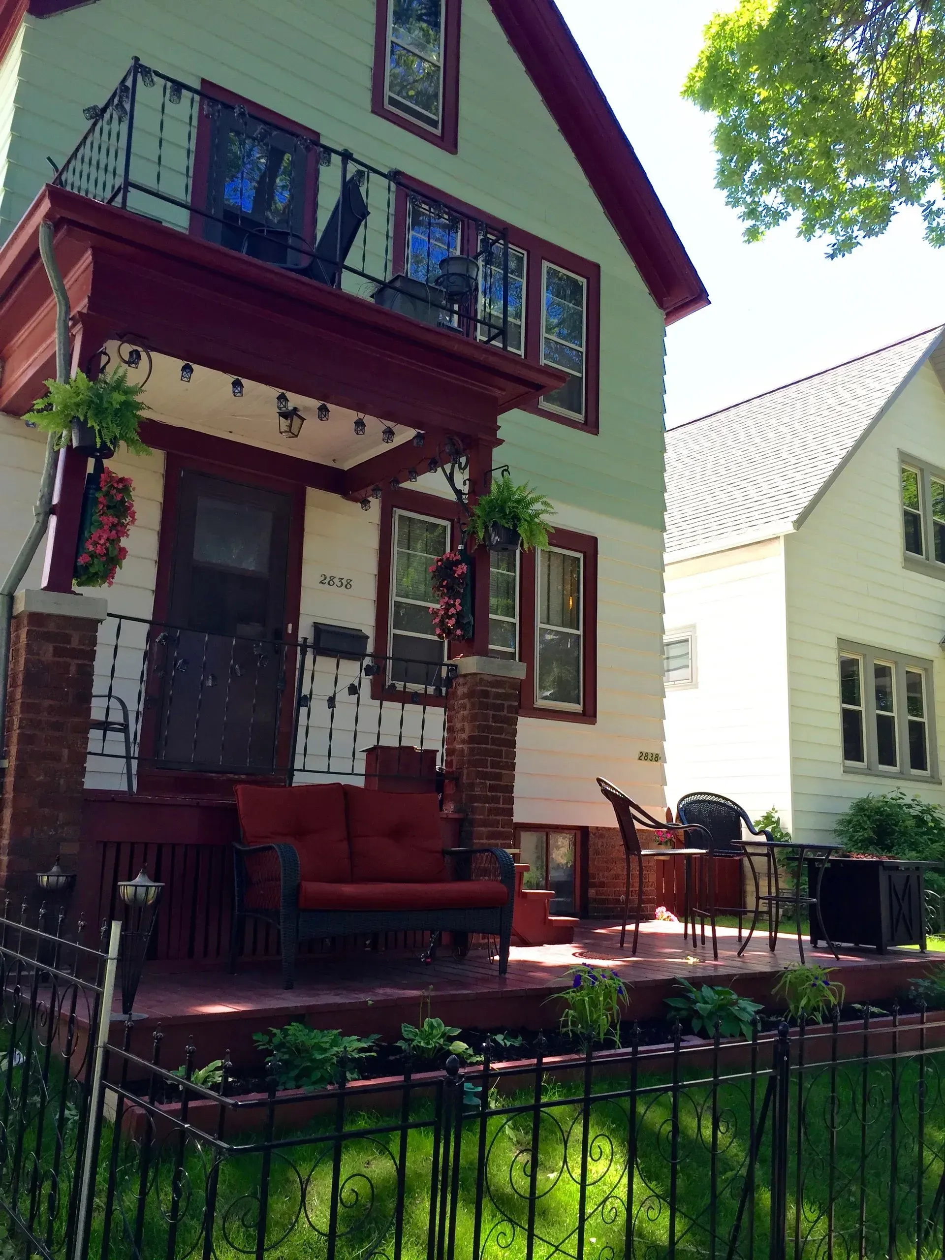 Two-story house with a red porch and accents, a small balcony, and a neighboring white house.
