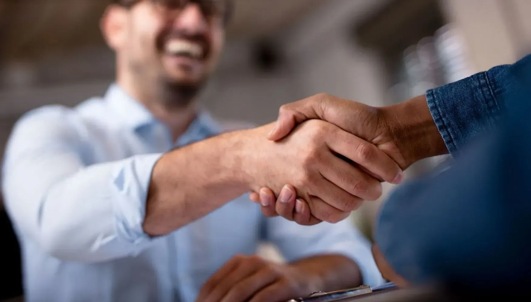 Man in light blue shirt shaking hands with person in blue denim, smiling.