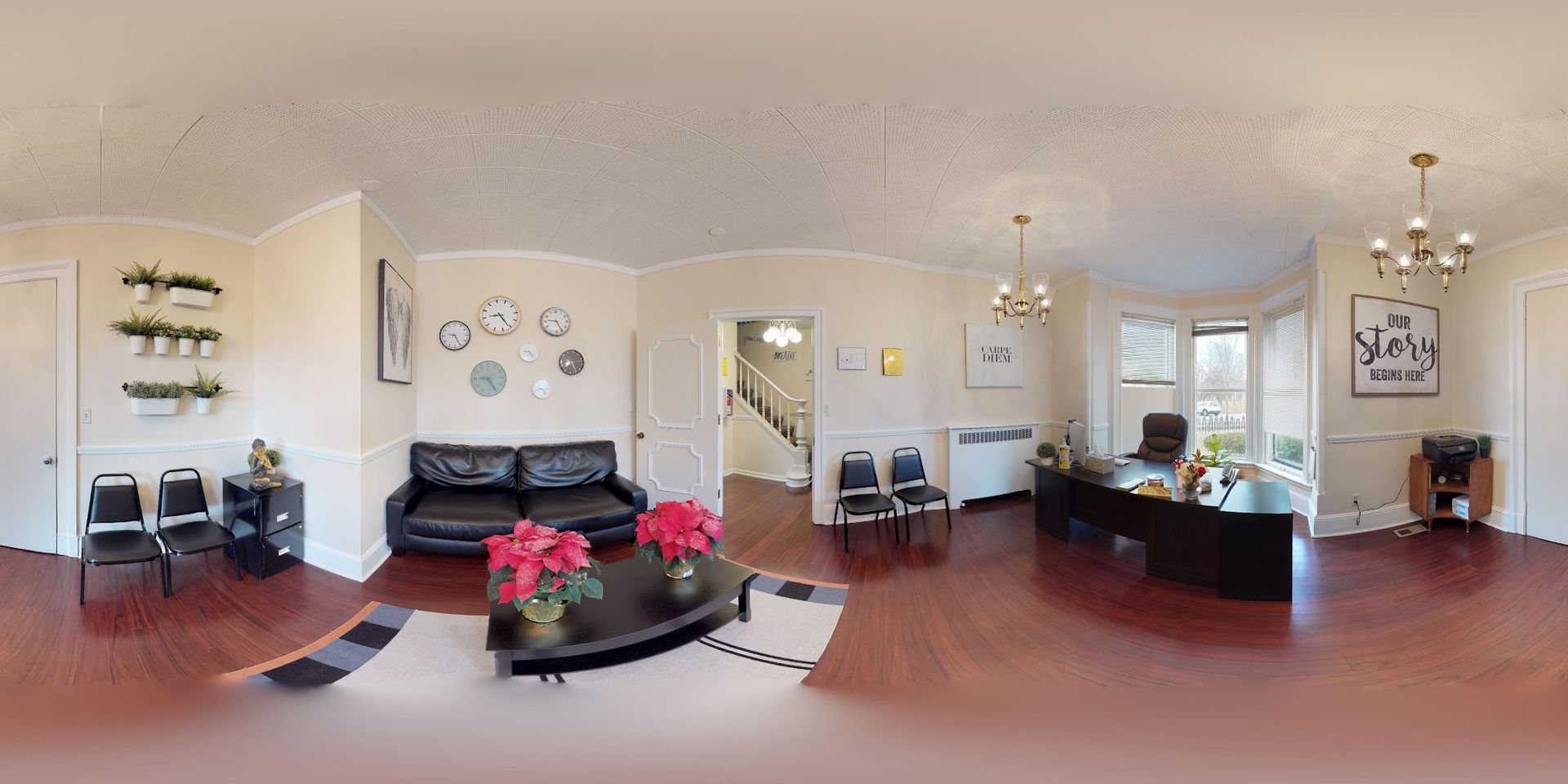 Reception area with black sofa, chairs, and a long desk.  Potted plants, chandeliers, and decorative wall art.