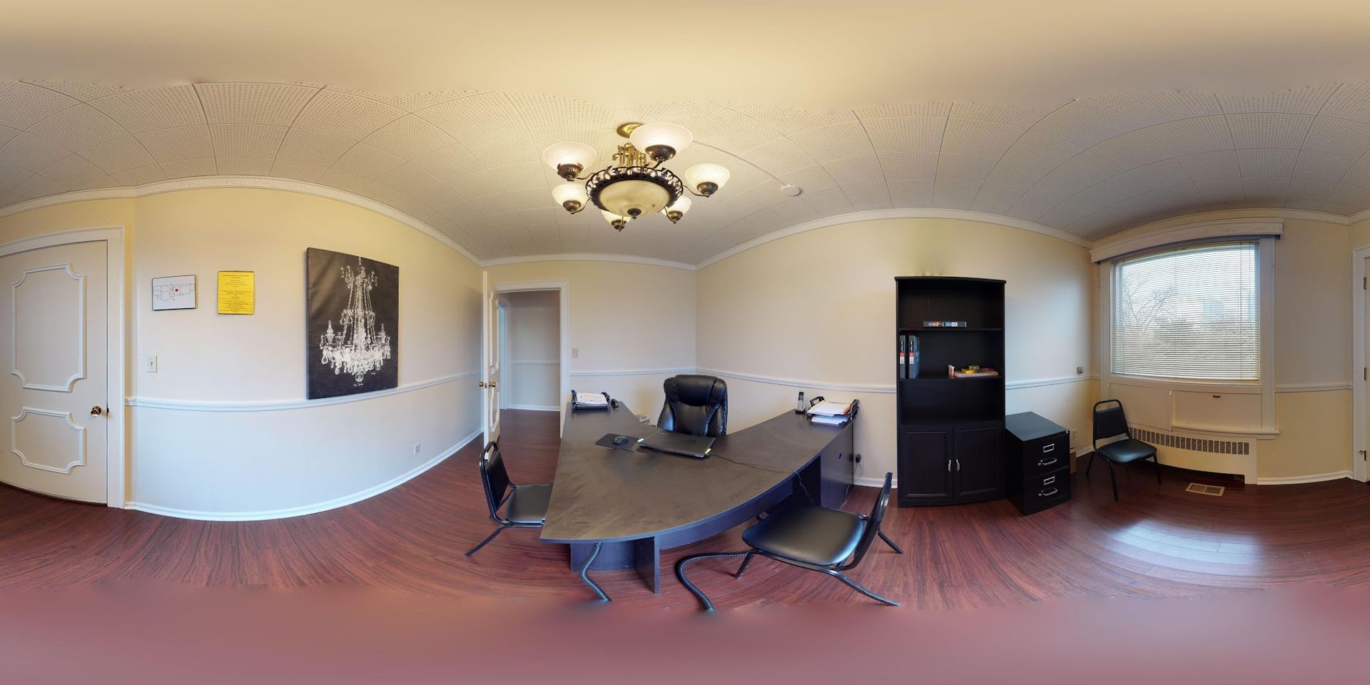 Office with a large dark desk, chairs, a black cabinet, and a chandelier. The walls are cream-colored.