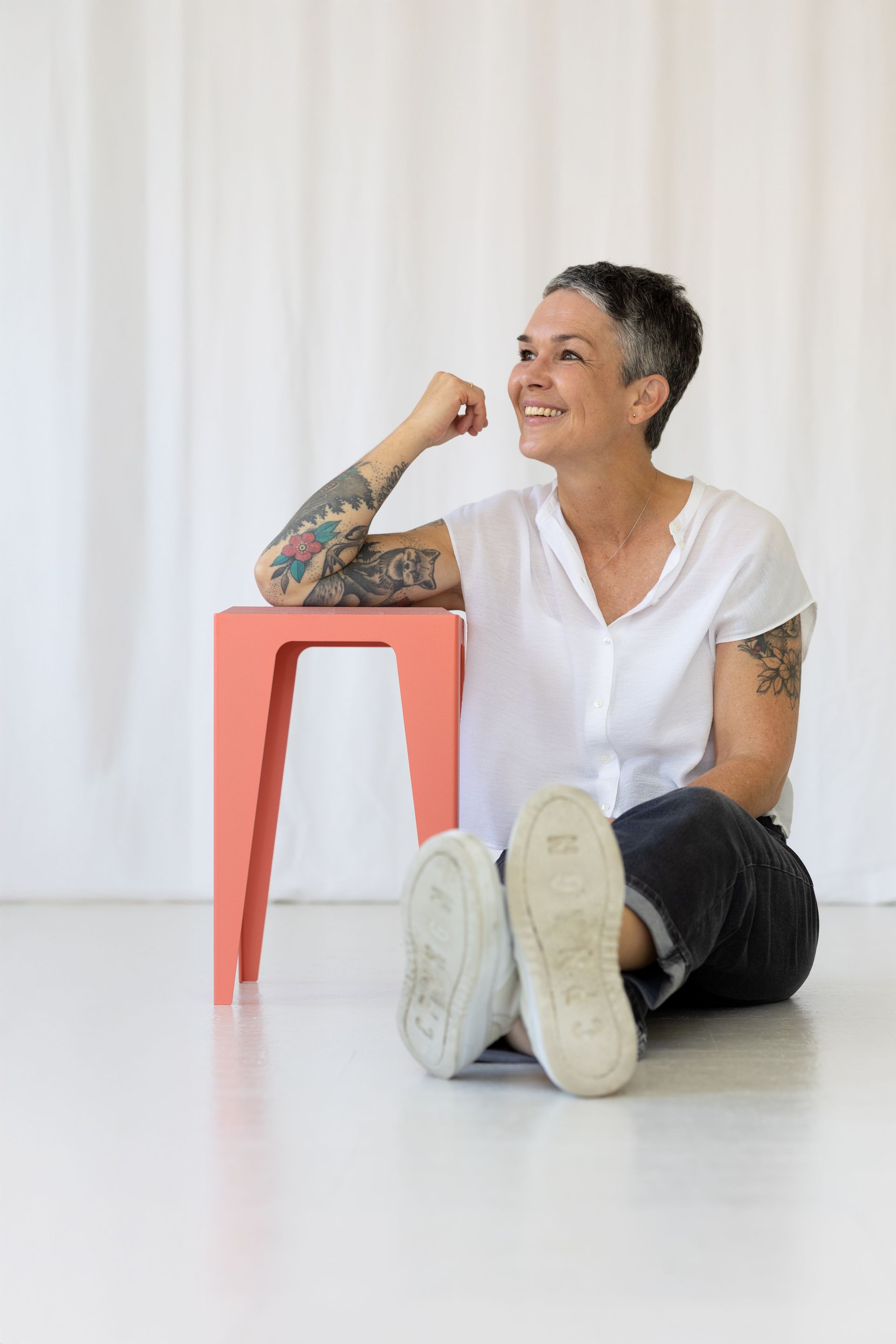 Frau sitzt auf Boden neben Hocker, weißes Oberteil, dunkle Hose, weiße Turnschuhe.Fotograf Tübingen. Fotograf Reutlingen.