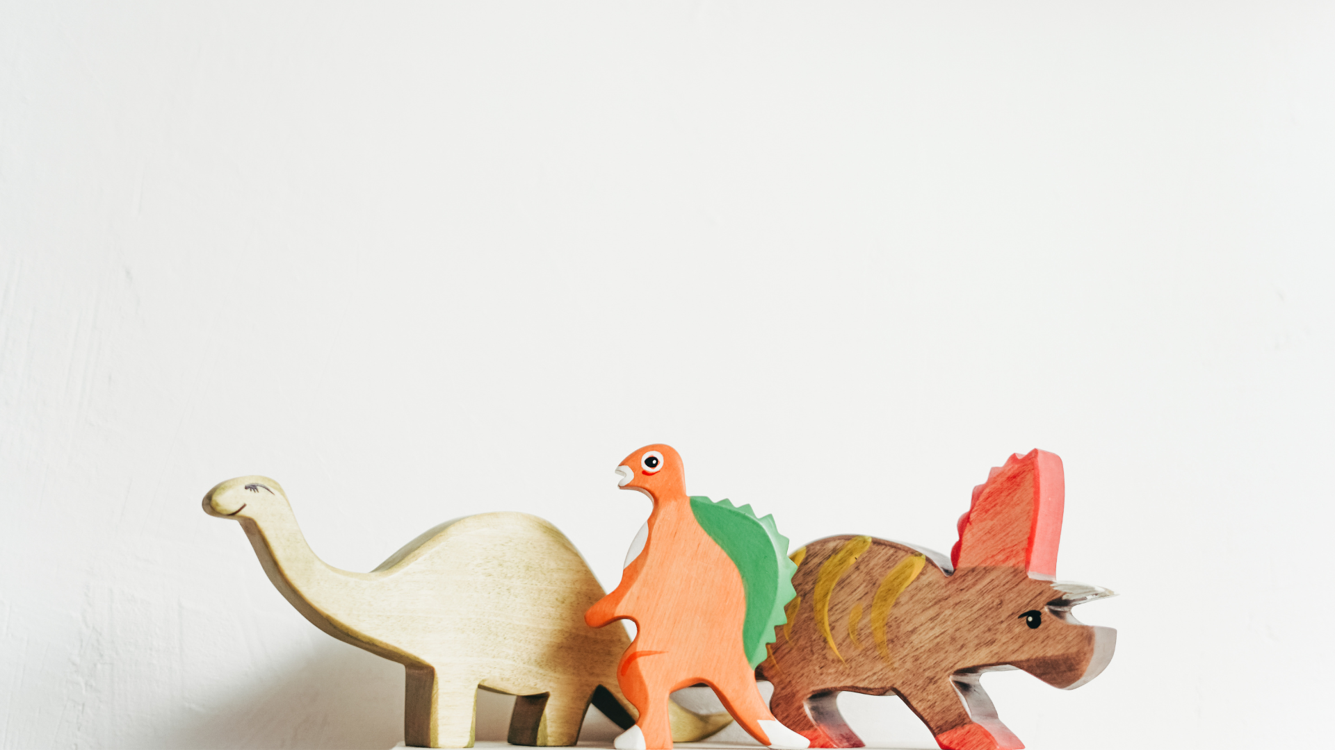 Three wooden dinosaurs are stacked on top of each other on a white surface.