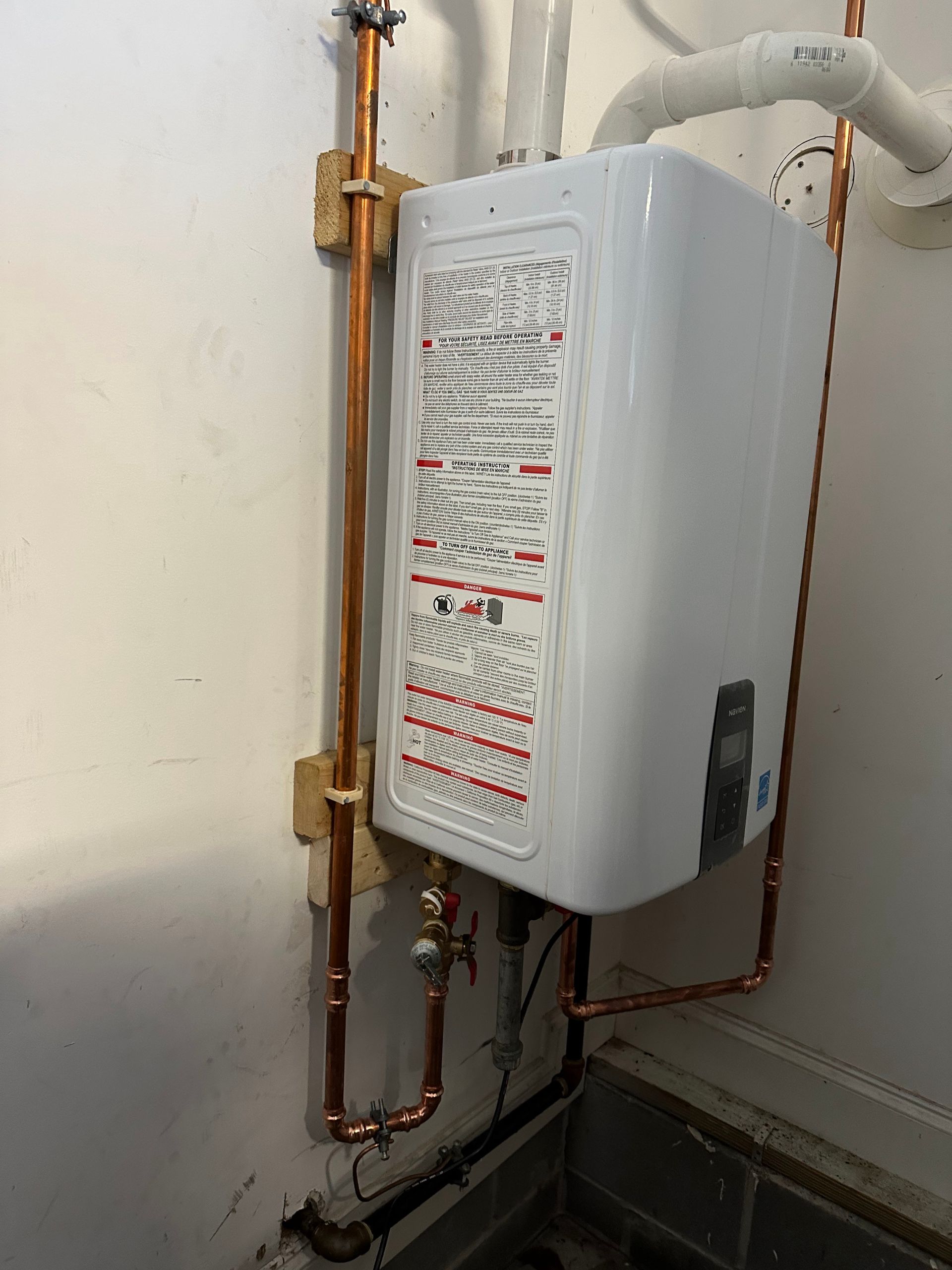 White tankless water heater installed on a white wall, with copper pipes.