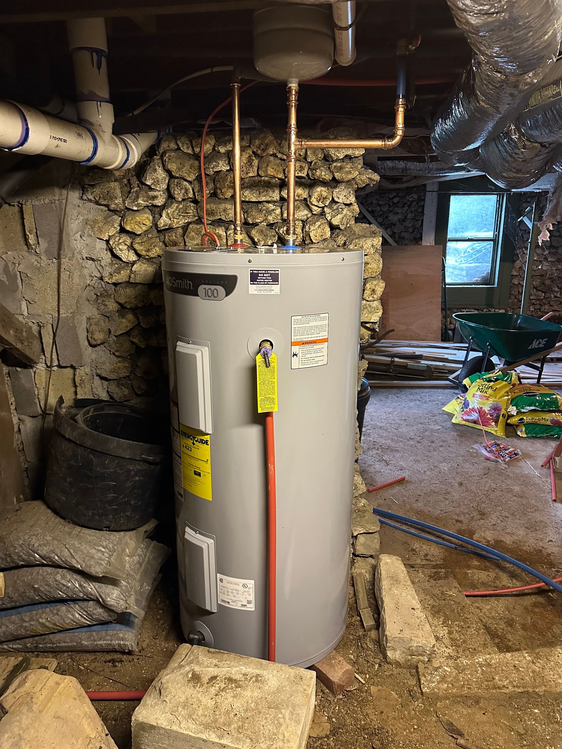 Water heater in a basement with stone walls and various pipes.