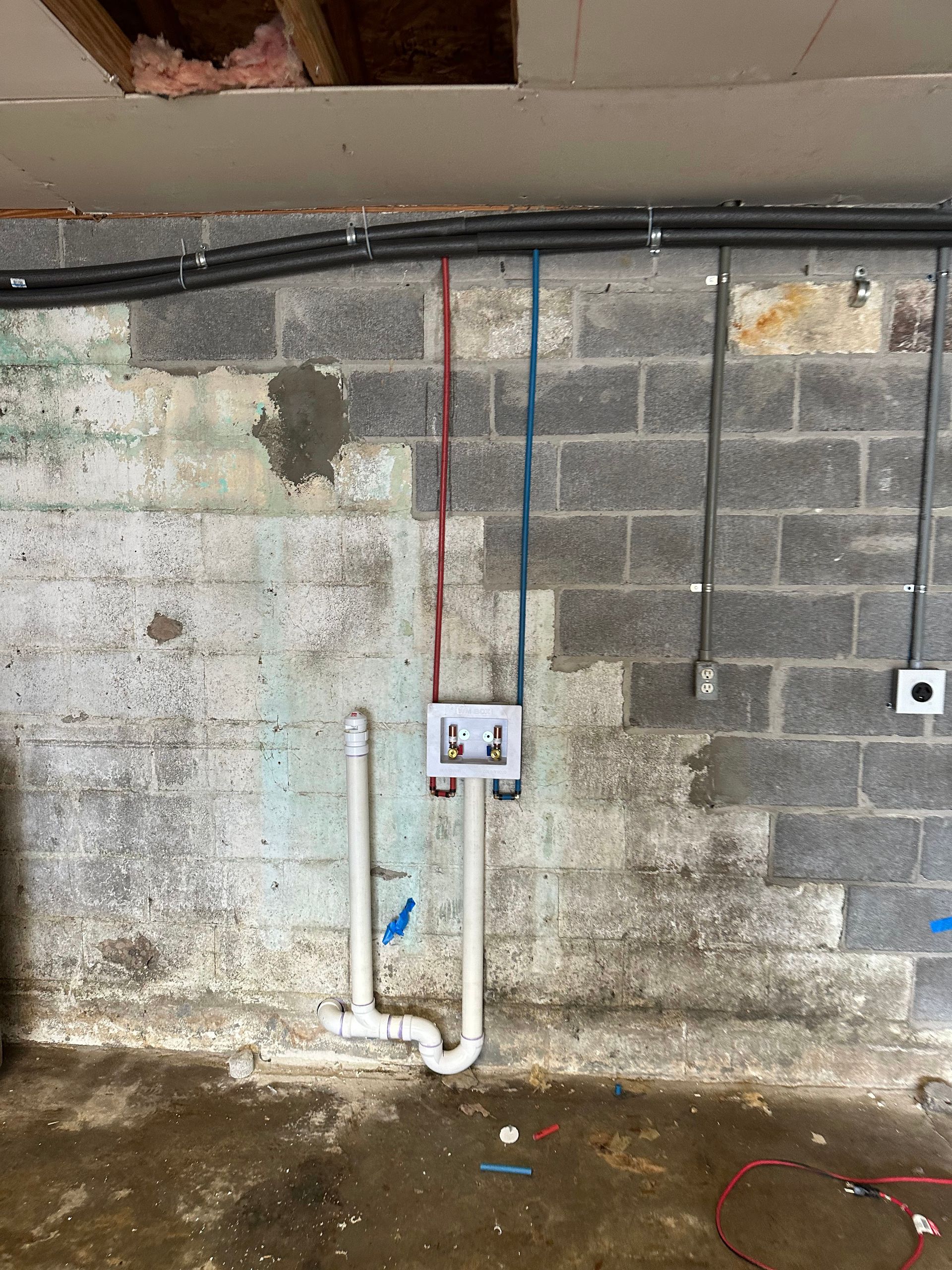 Laundry room wall with water pipes and electrical conduit running across cinder block.