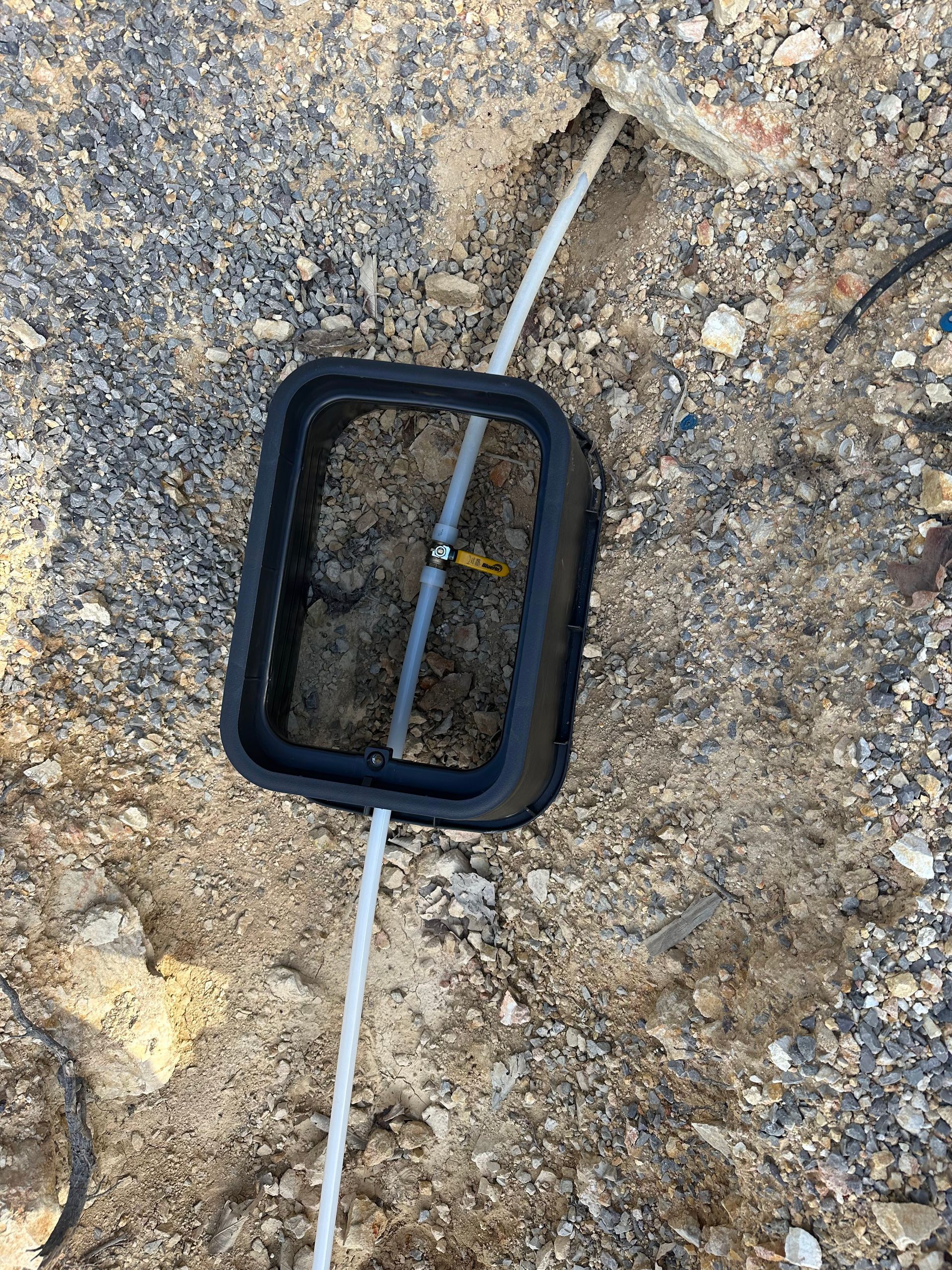 Black rectangular utility box in gravel, with white tubing.