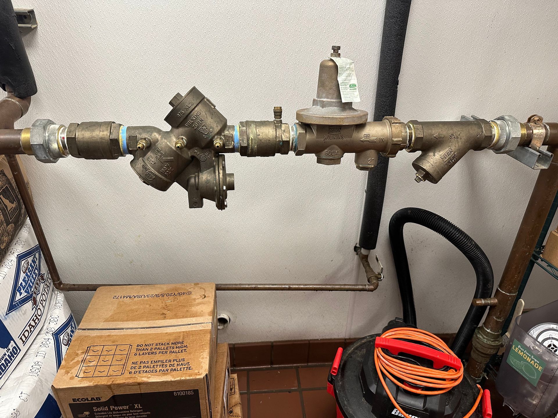 Water pipes with a pressure regulator and backflow preventer in a utility room.