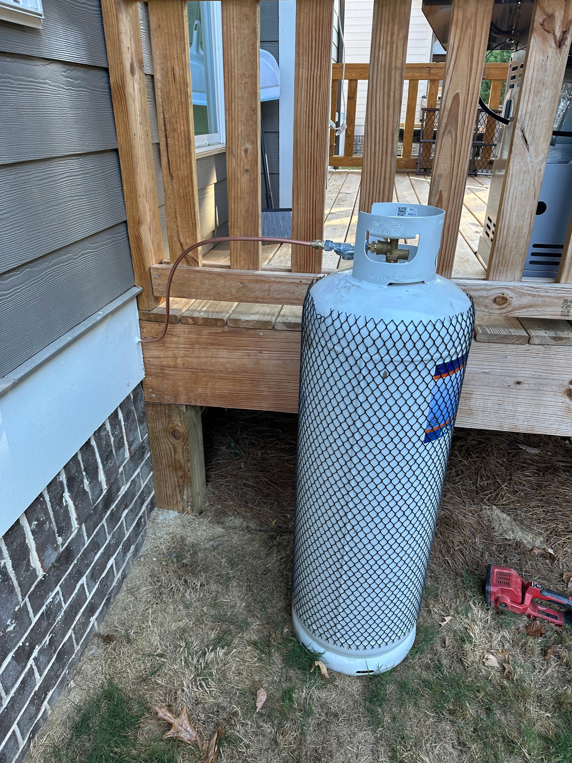 Propane tank next to wooden deck, near house with gray siding and brick.
