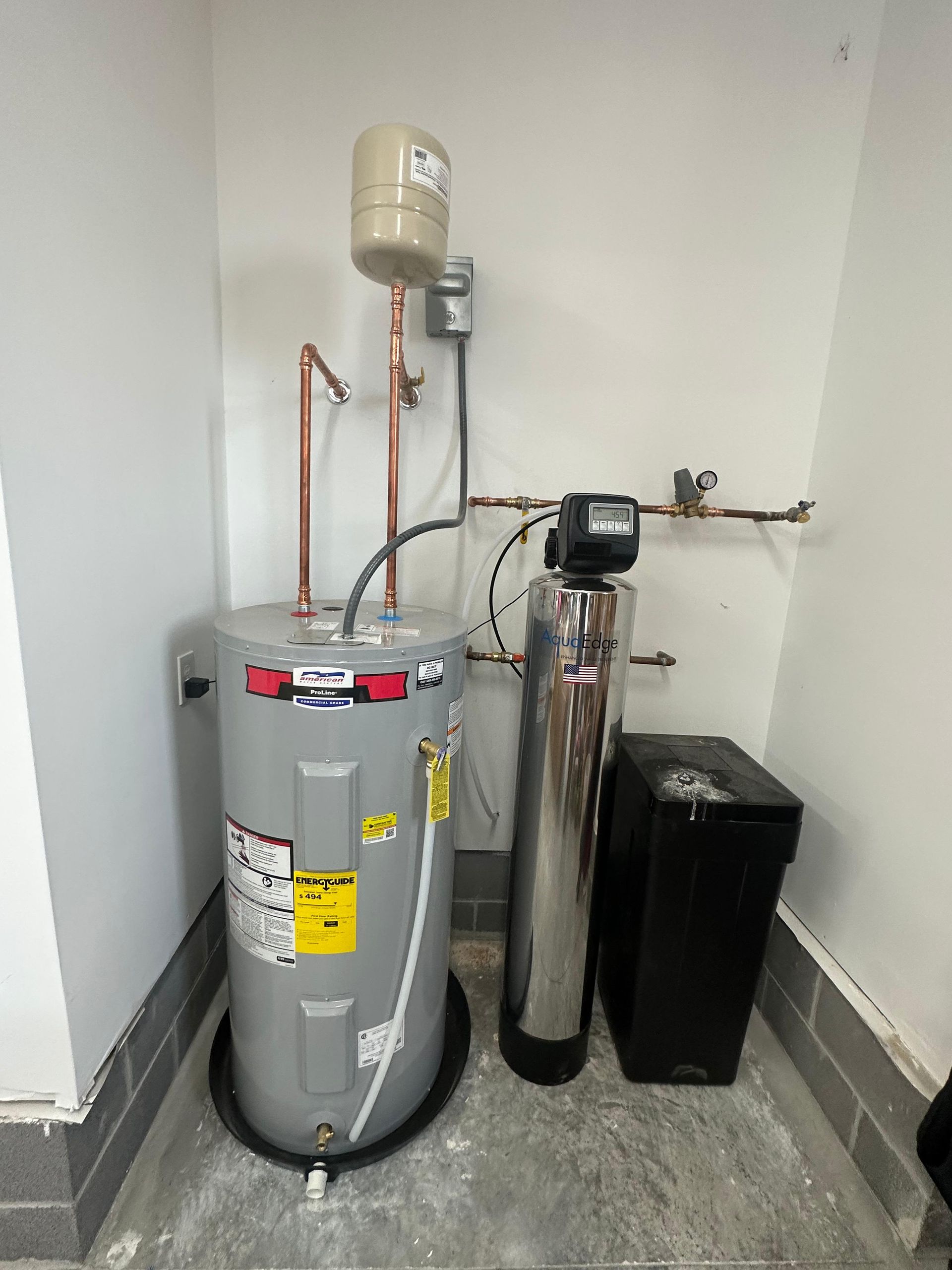 Water heater, water softener, and expansion tank in a corner. Gray and silver appliances.