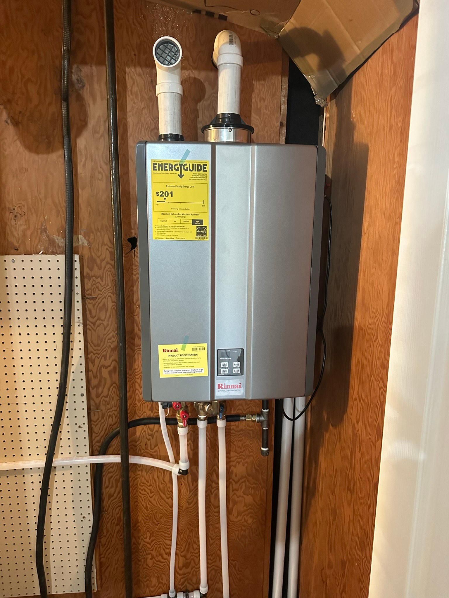 Tankless water heater, mounted on wood wall, with exhaust pipes and water lines.