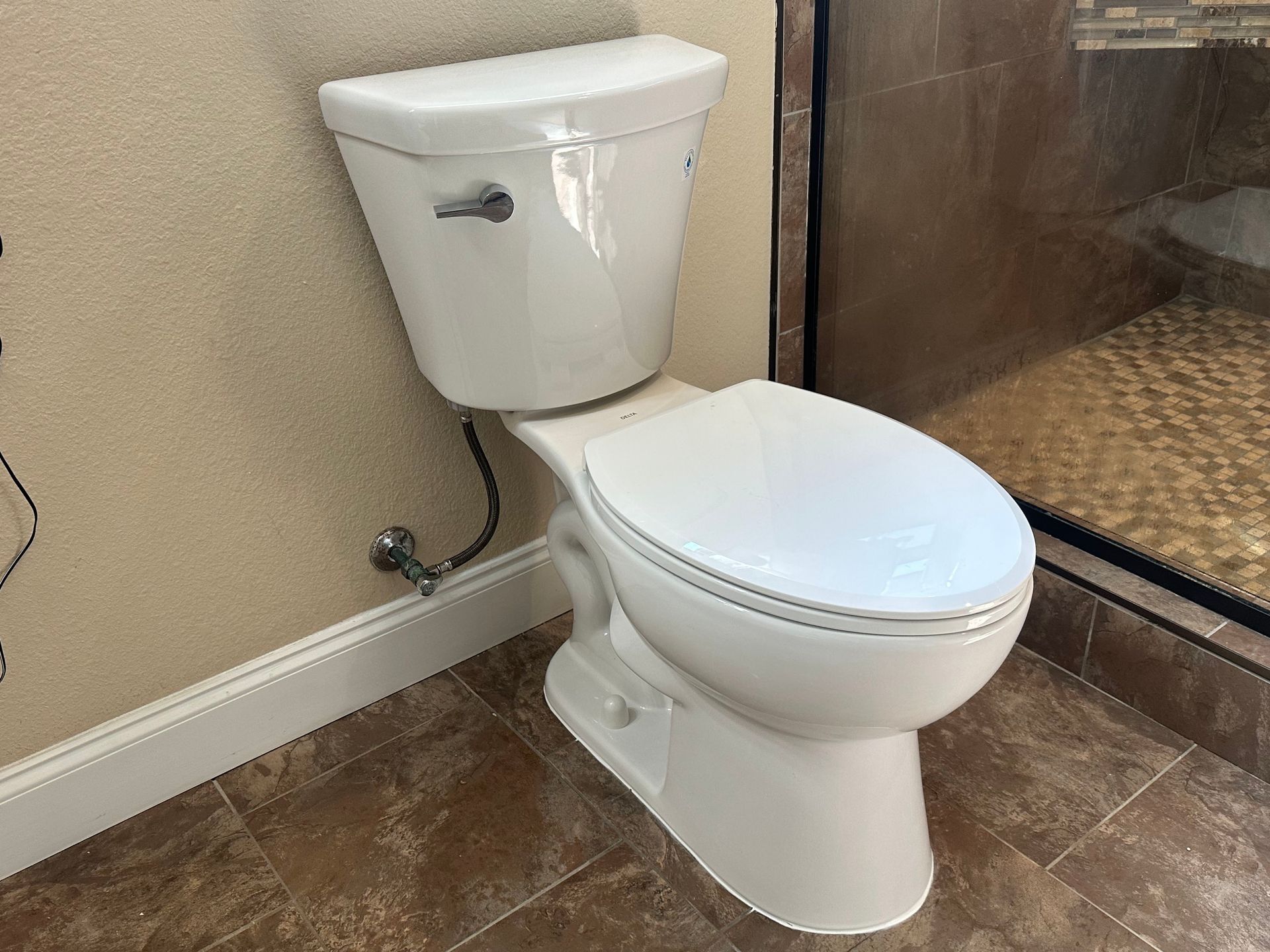 White toilet in a bathroom, next to a shower. Brown tile flooring.