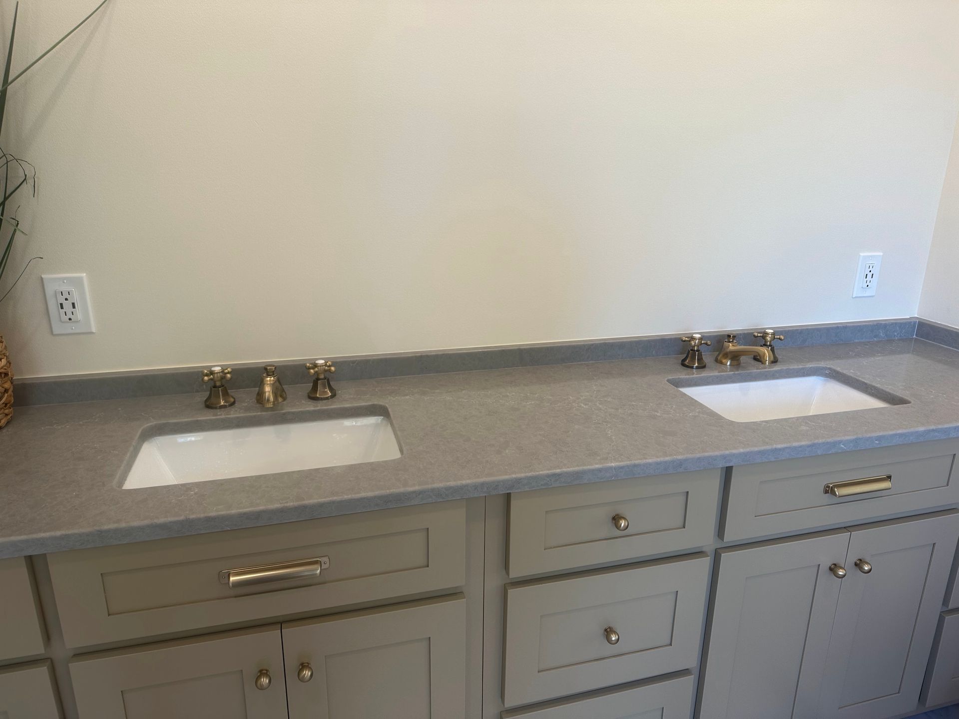 Light gray bathroom vanity with two sinks, gold fixtures, and tan cabinets.