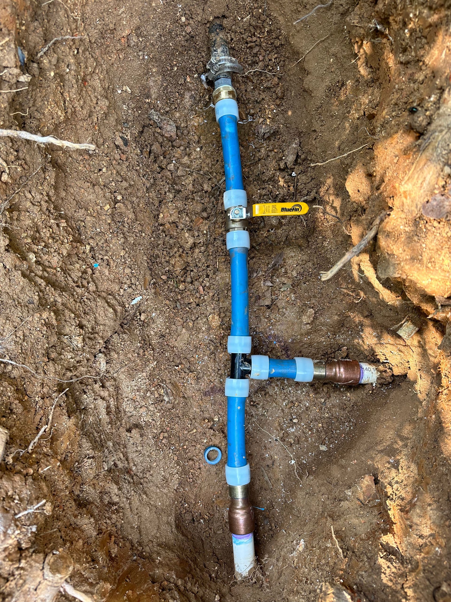 Blue water pipe with a brass valve and copper fitting in dirt.