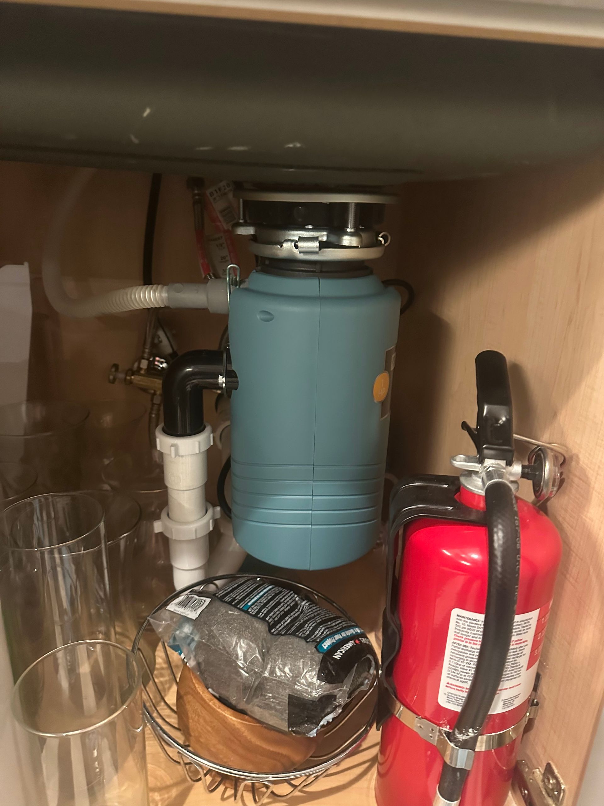 A blue garbage disposal under a kitchen sink next to a red fire extinguisher.