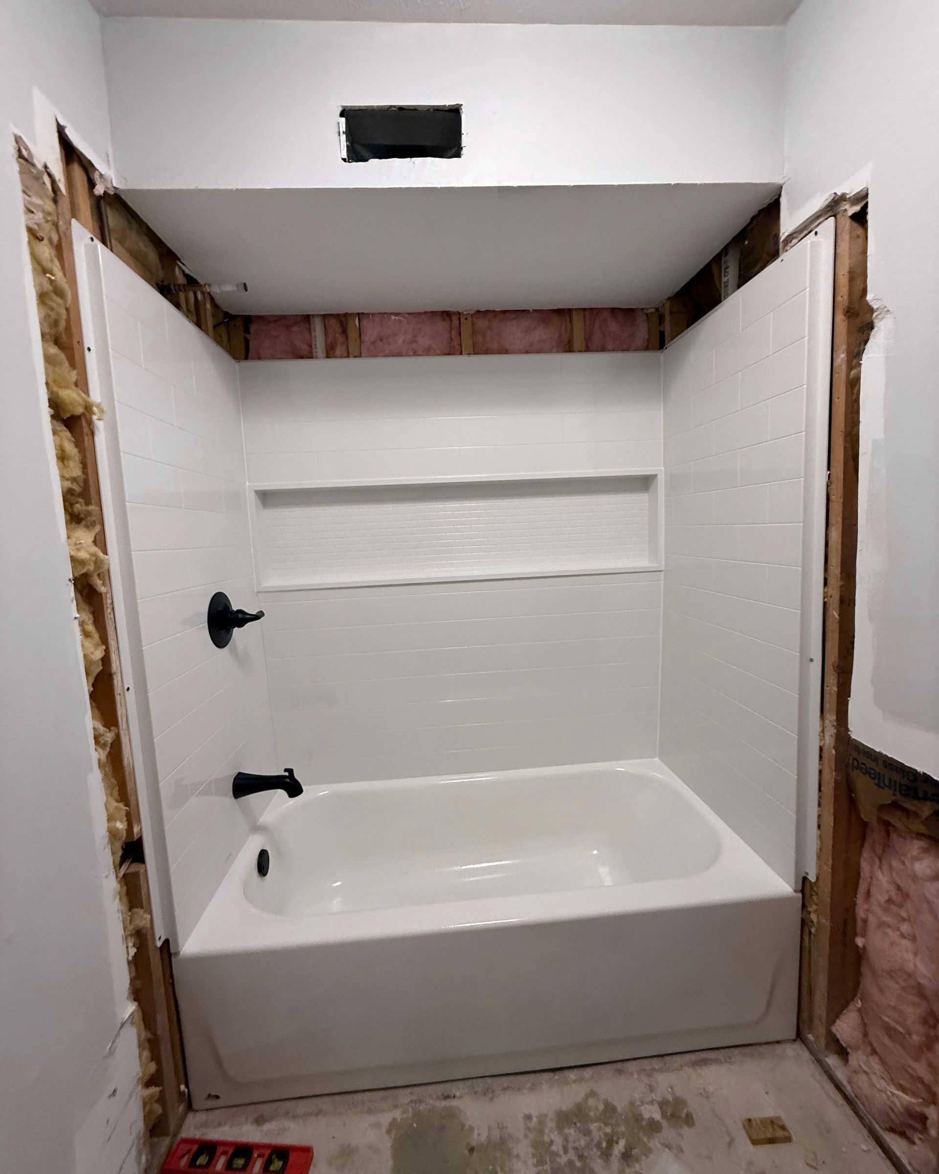 White tub and surround installed in a bathroom renovation, with exposed wall studs.