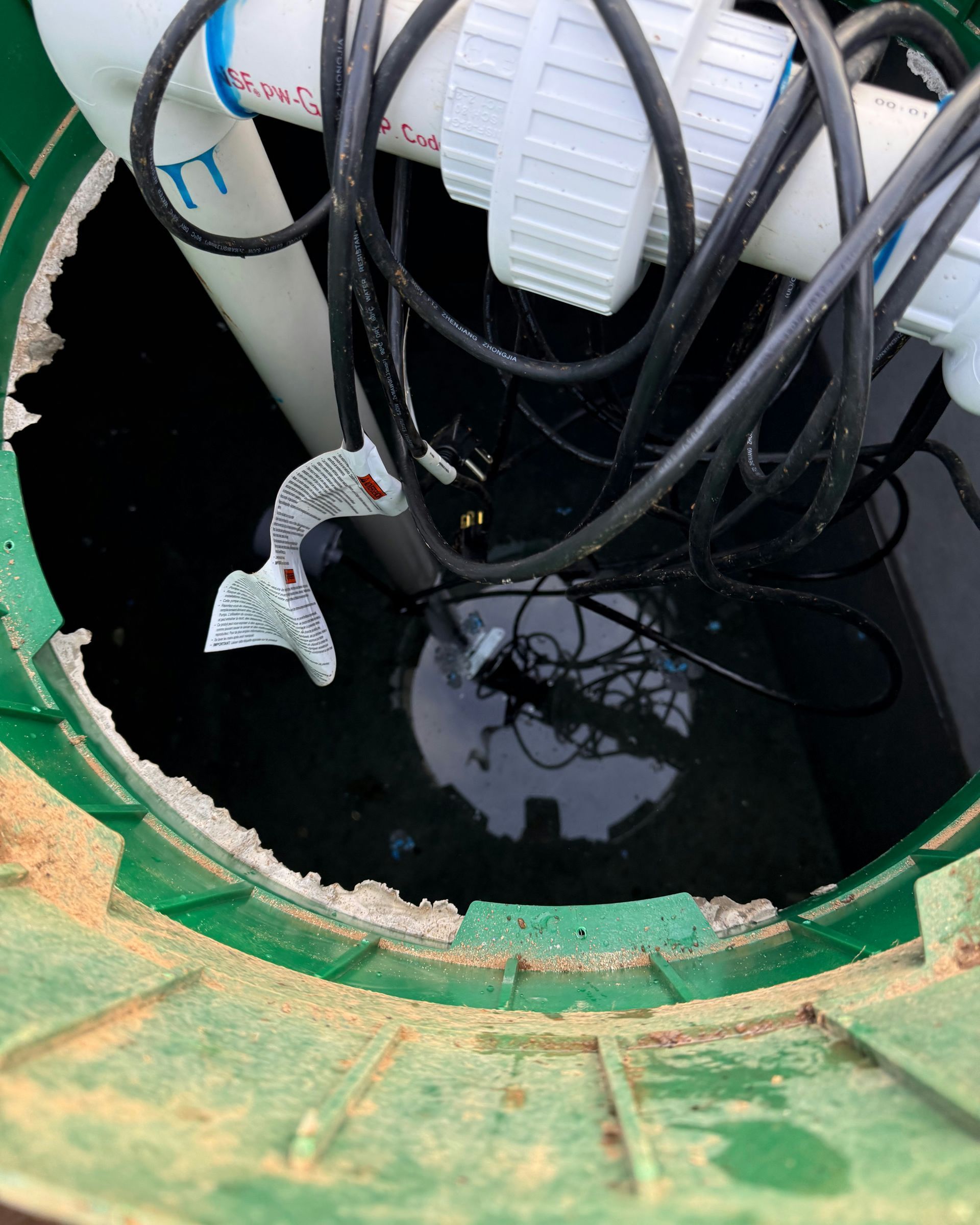 Green well, showing water inside, PVC pipes, electrical cables, and damage around the opening.