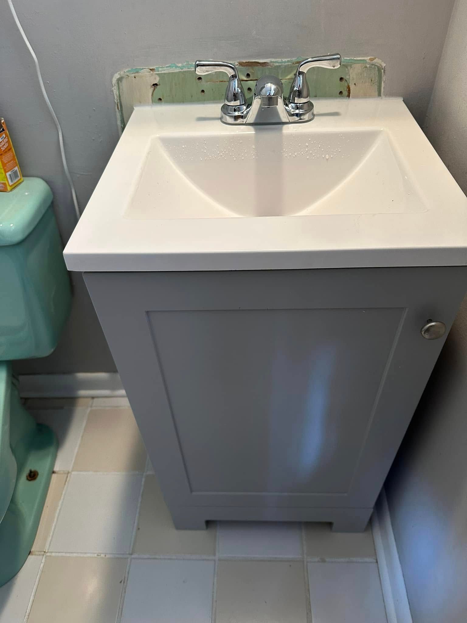 Gray vanity with white sink in a bathroom next to a turquoise toilet.