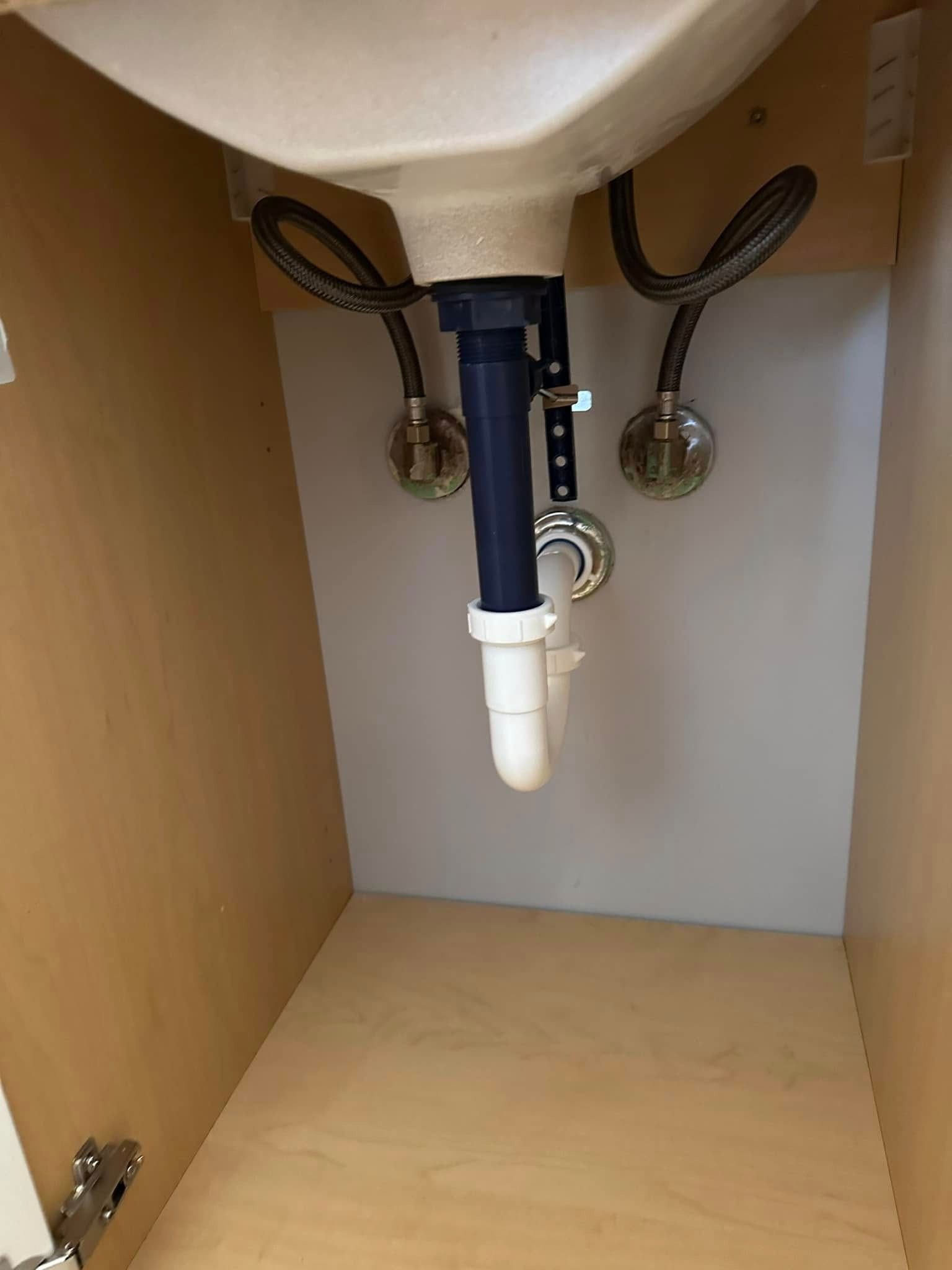 Underside of a bathroom sink inside a cabinet with plumbing and water supply lines visible.
