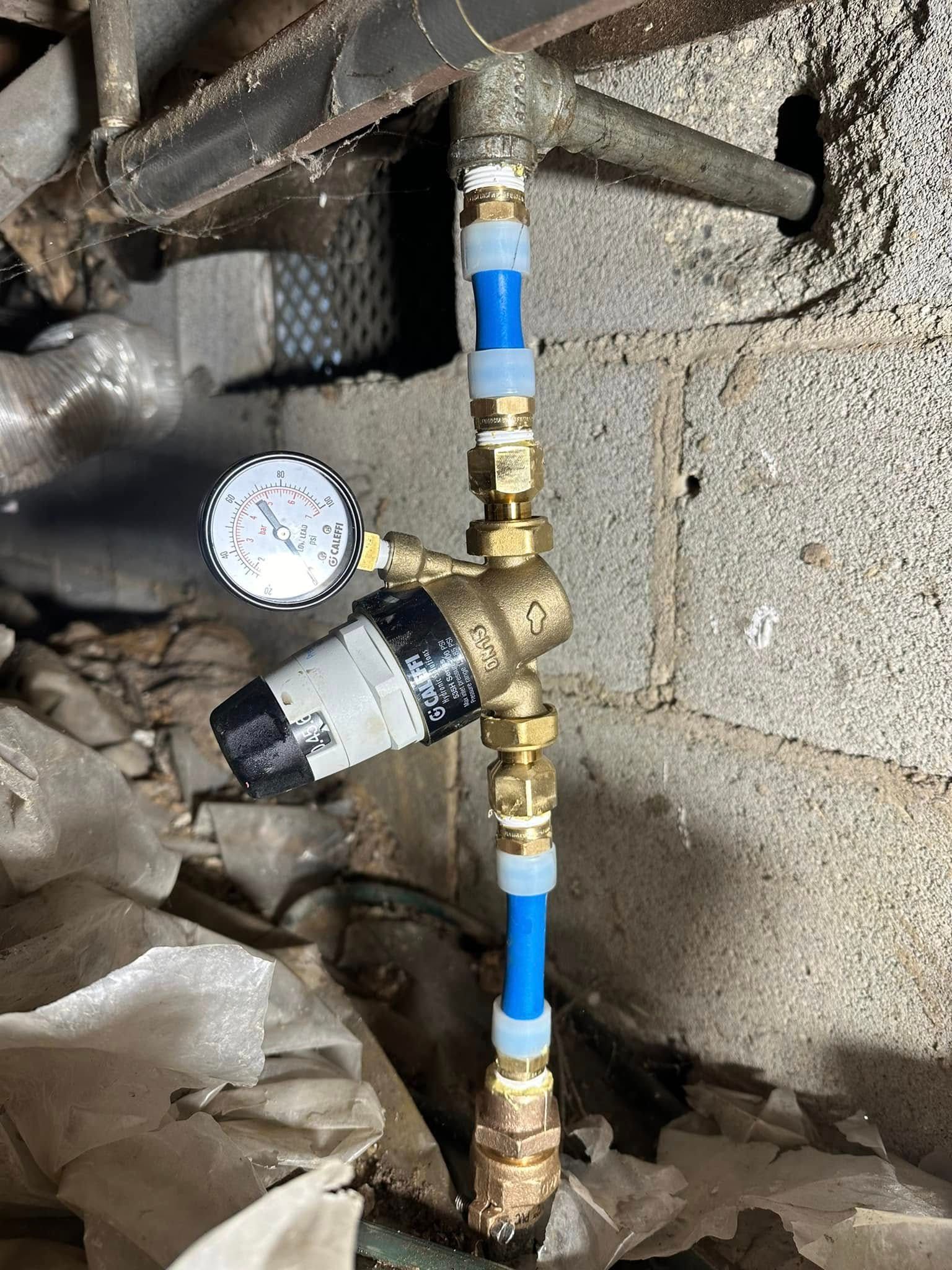 Water pressure regulator with gauge installed on blue PEX piping in a basement.