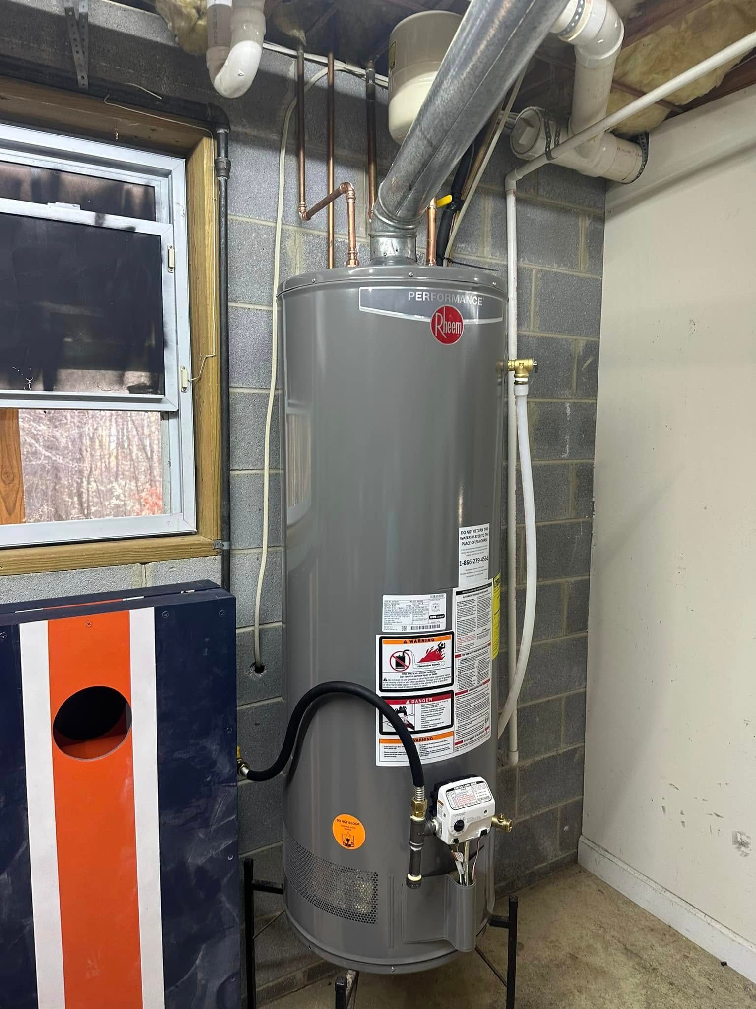 A tall gray water heater next to a cinder block wall, with pipes and a window nearby.