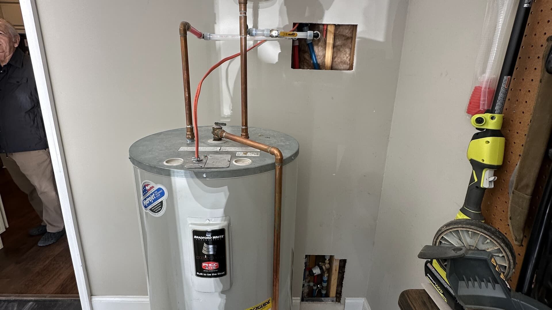 A water heater with copper pipes installed in a utility room. A person stands in the doorway.