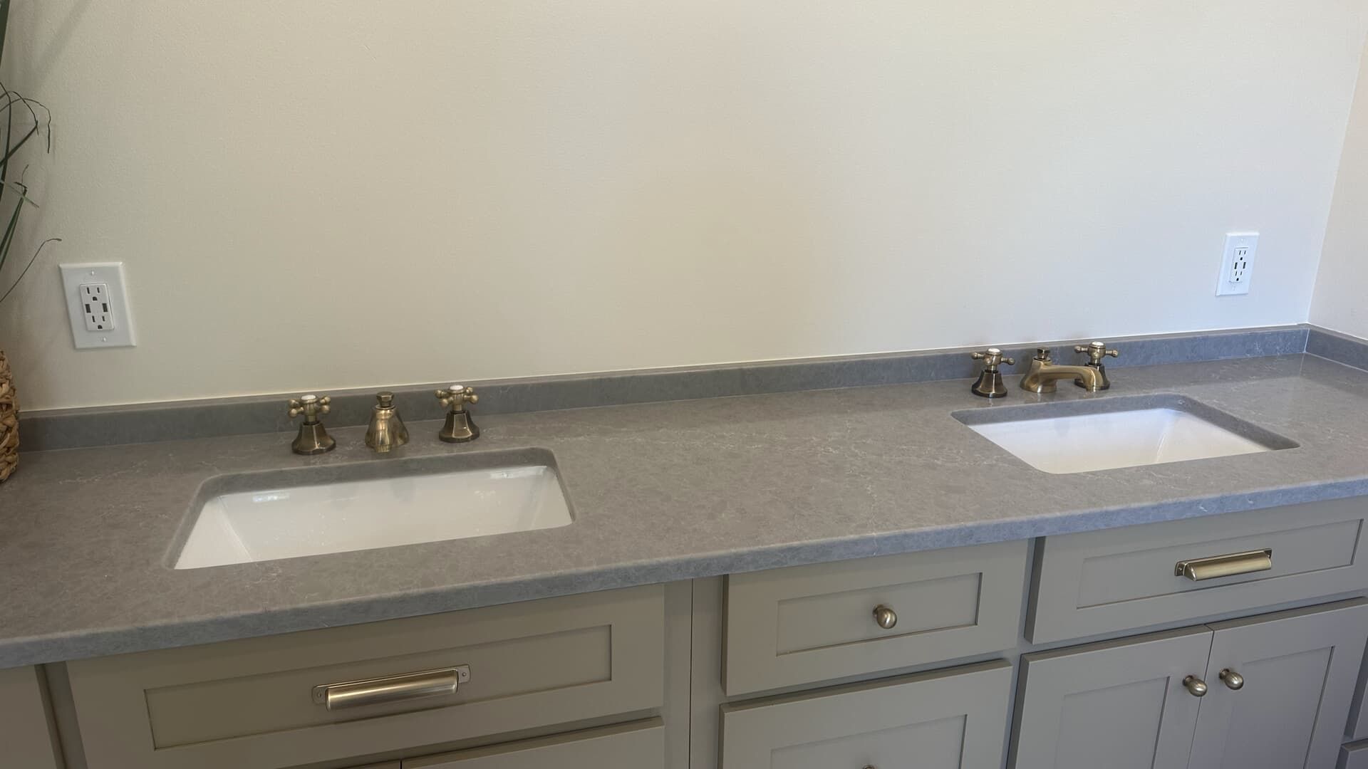 Double bathroom vanity with gray countertop, white sinks, gold fixtures, and gray cabinets.