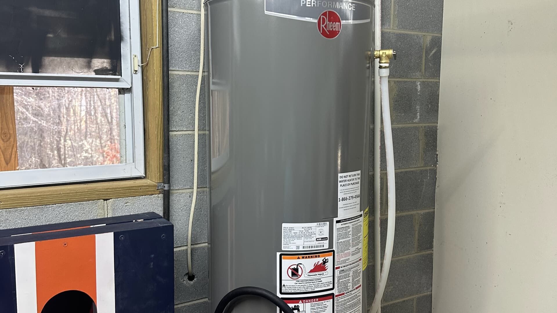 Gray water heater in a corner of a room, against a brick wall.
