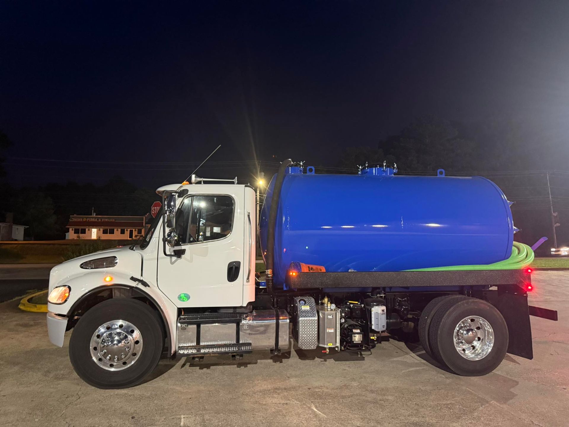 White sanitation truck with a blue tank parked at night.