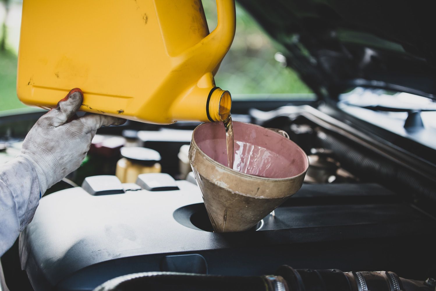 A person is pouring oil into a funnel into a car engine.