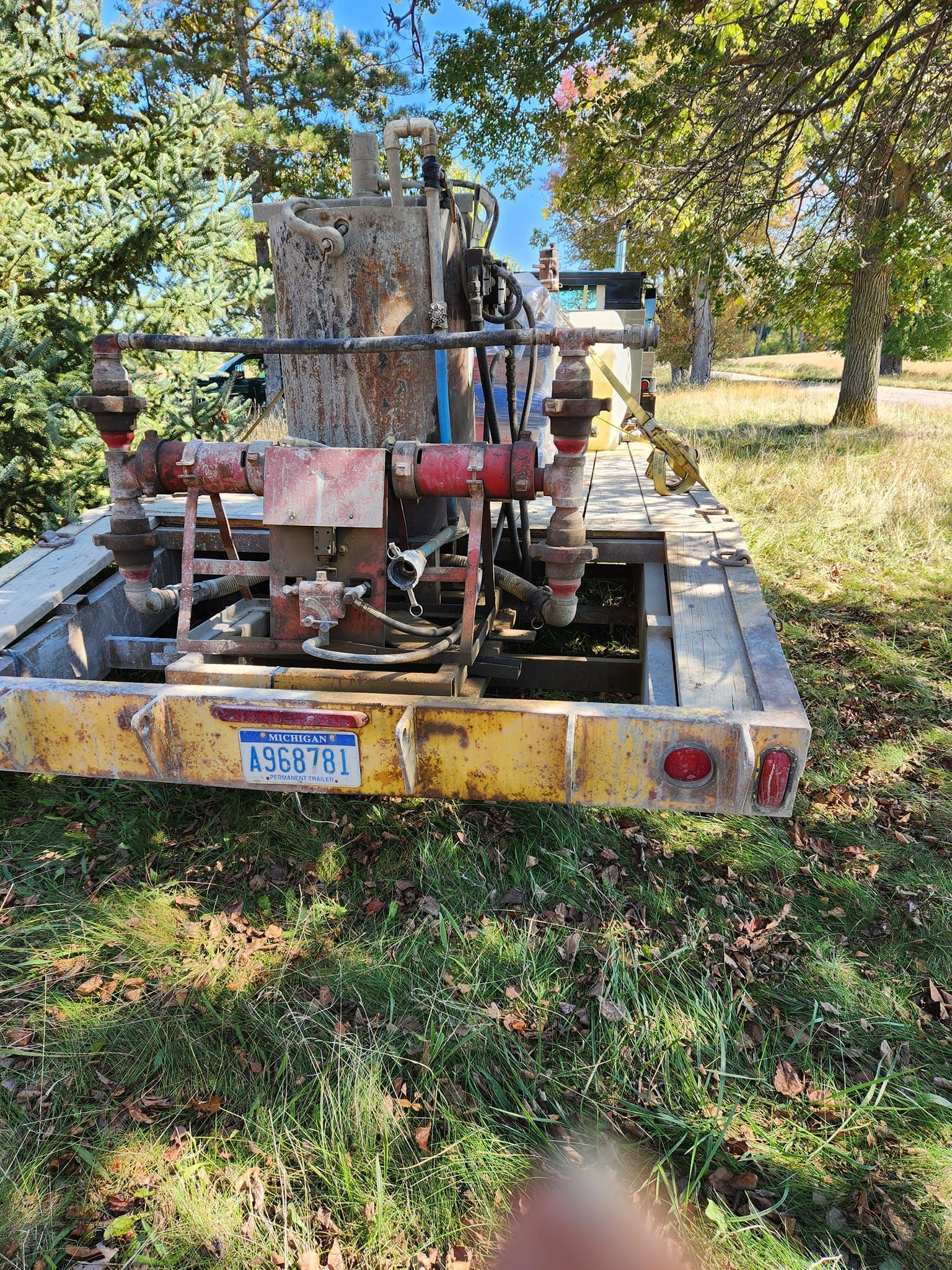A yellow trailer with a lot of pipes on it is parked in a grassy field.