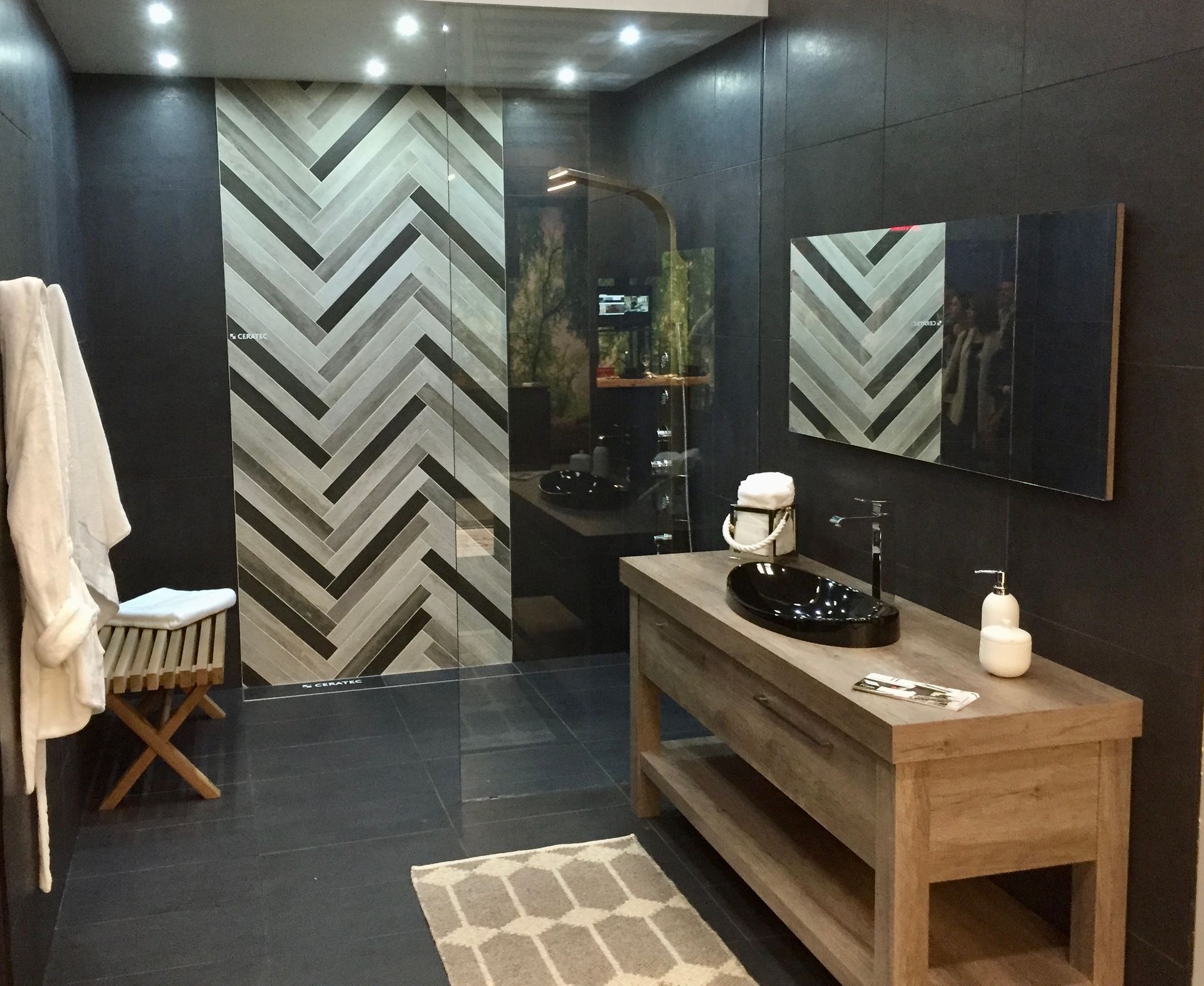 Salle de bain moderne avec murs gris, vanité en bois et douche en carrelage à chevrons.