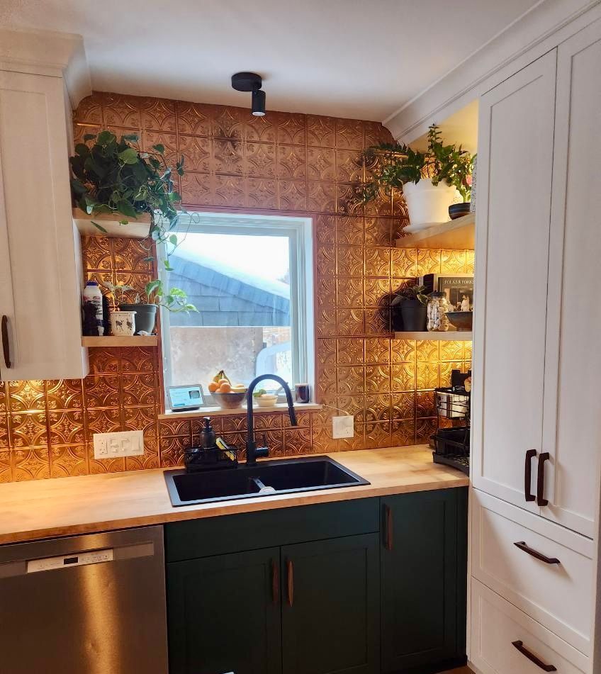 Cuisine avec armoires vertes, dosseret en cuivre et étagères blanches avec plantes.