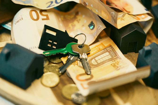 House keys on a pile of cash with small house models.