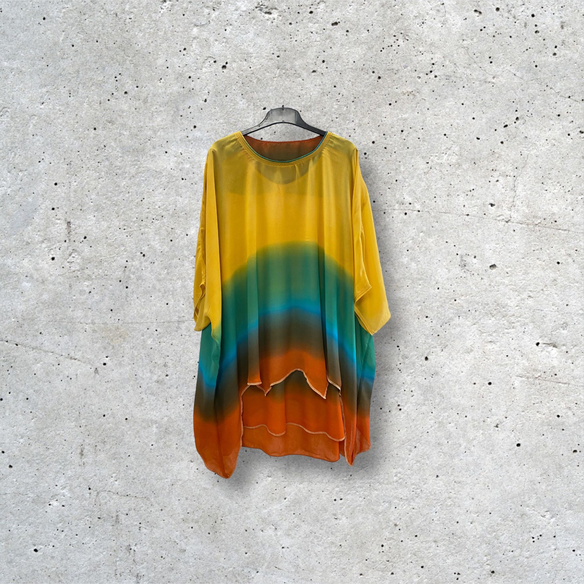 Une chemise colorée est accrochée à un cintre contre un mur en béton