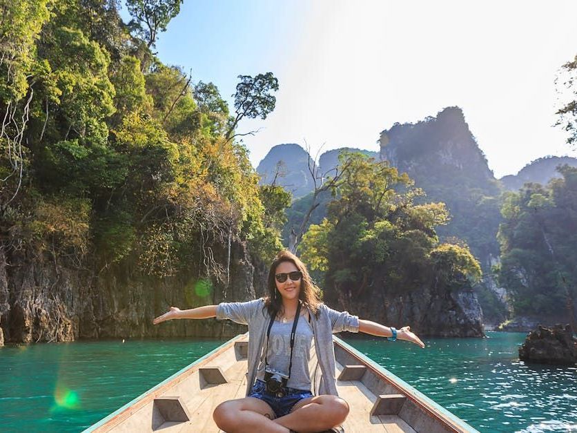 A woman is sitting in a boat on a lake with her arms outstretched.