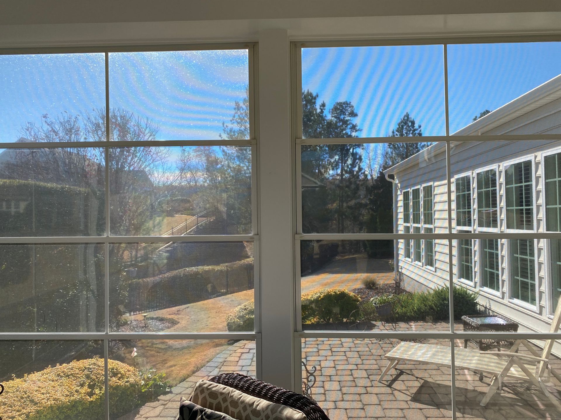 View from a screened porch. Outside is a sunny yard with a house and path.