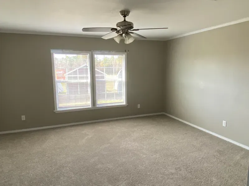 An empty room with a ceiling fan and two windows.