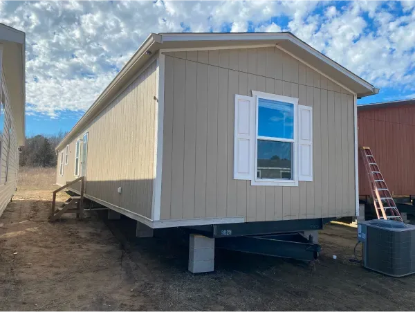 A mobile home is sitting on top of a trailer in a dirt field.