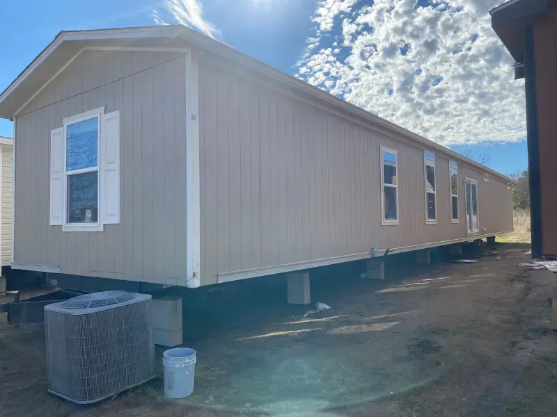 A mobile home is parked in a dirt lot next to a house.