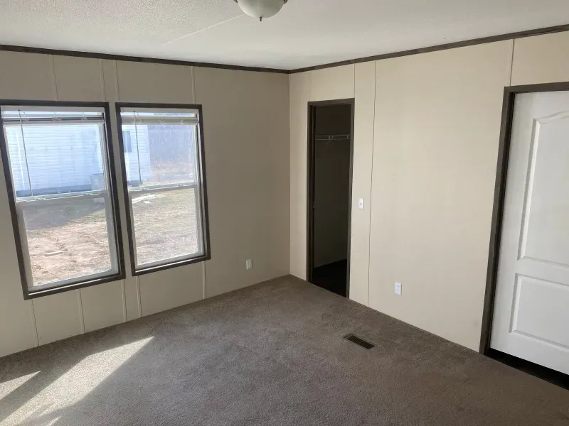 An empty room with two windows and a door in a mobile home.