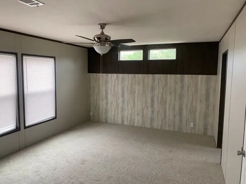 An empty room with a ceiling fan and two windows.