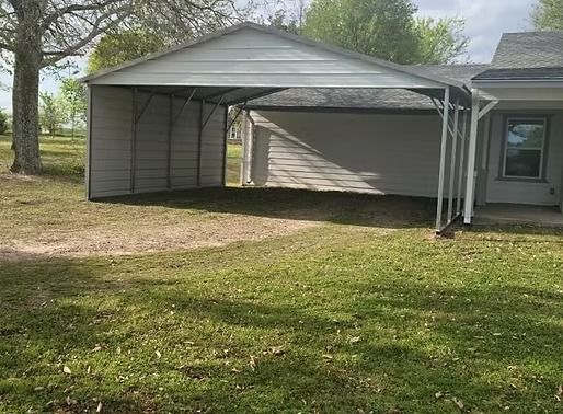 A carport is sitting in the grass in front of a house.