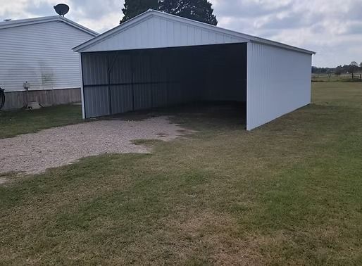 A white garage is sitting in the middle of a grassy field.