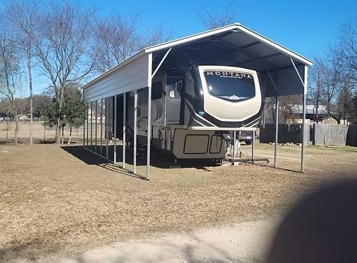 A rv is parked under a carport on a sunny day